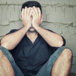 Depressed young man sitting on the floor and covering his face w